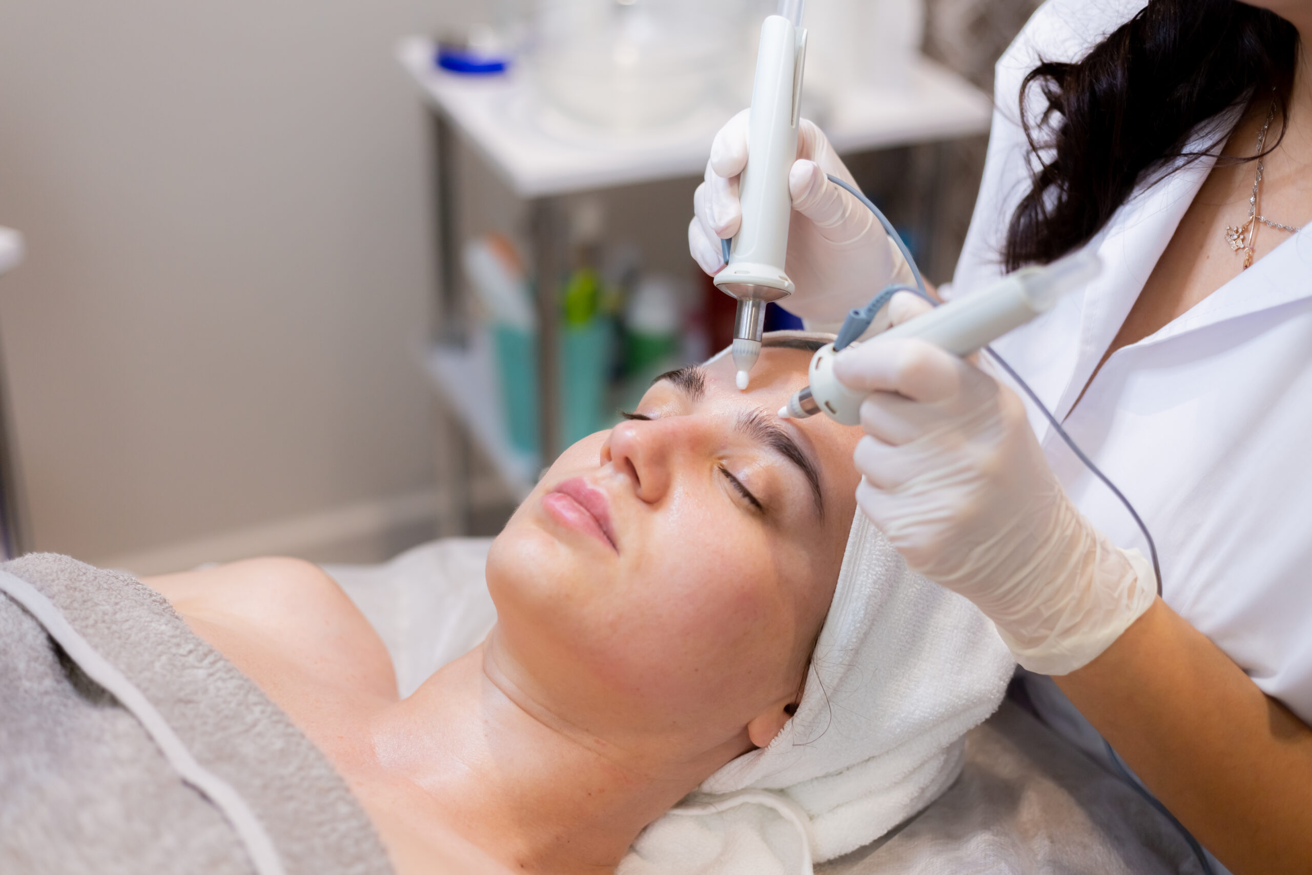 A young beautiful girl lies on the beautician's table and receives procedures with a professional apparatus for skin rejuvenation and moisturizing